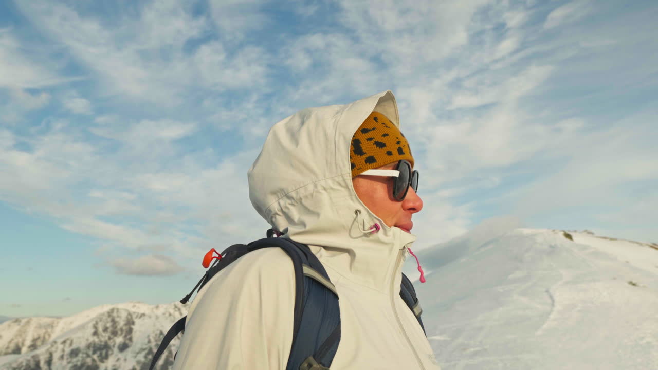 Parallax shot of caucasian woman on top of snowy mountain looking at the beautiful landscape, gimbal shot