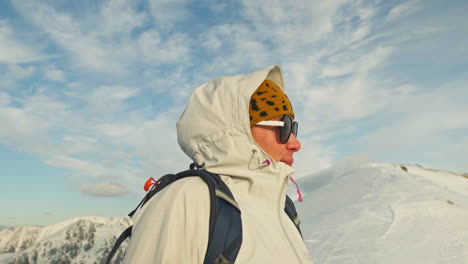 parallax shot of caucasian woman on top of snowy mountain looking at the beautiful landscape, gimbal shot
