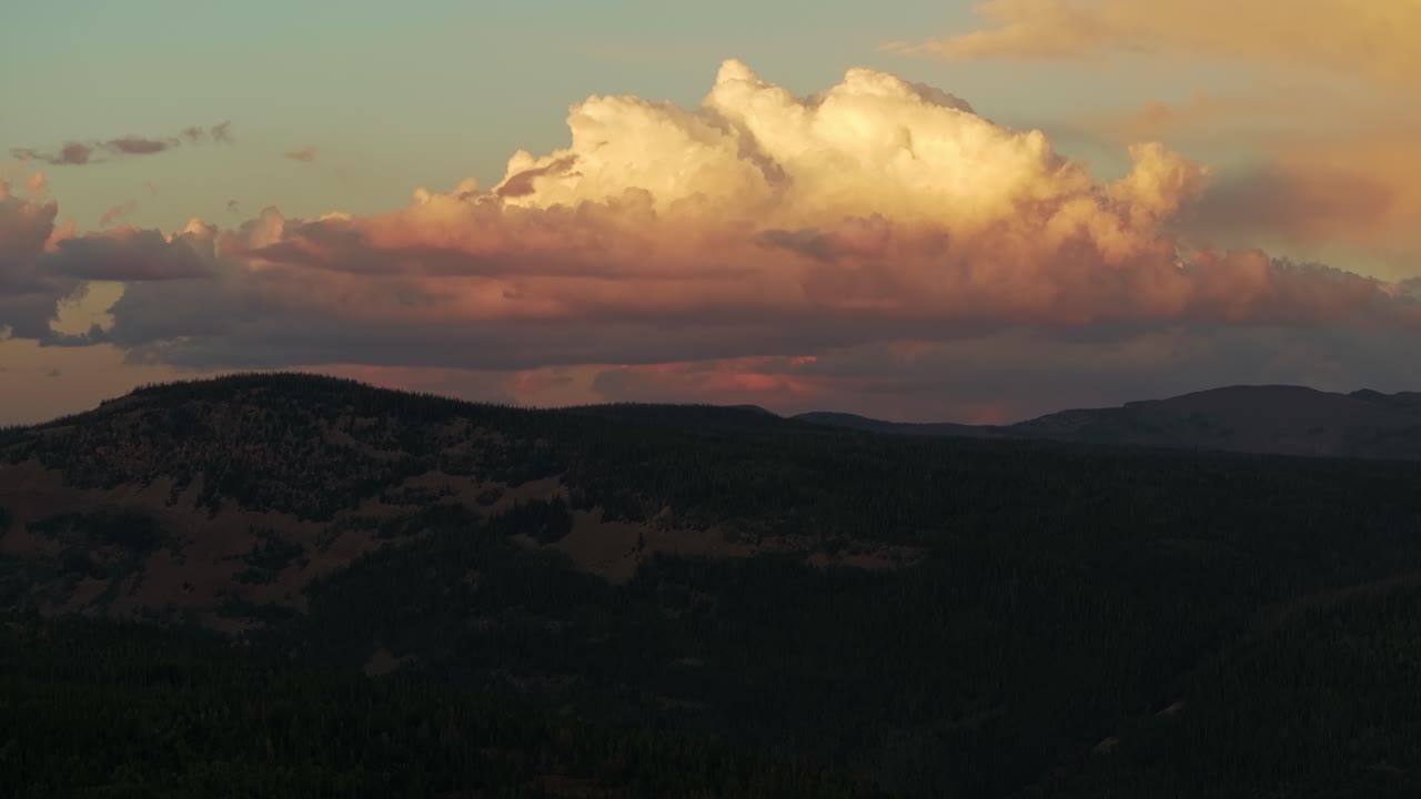 Drone wide shot of the Uinta-Wasatch-Cache National Forest in Utah during a summer sunset, pine trees, Provo River, mountain peaks and clouds rising above the valley