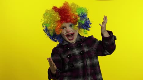 little child girl clown in colorful wig making silly faces, fool around, smiling, dancing. halloween