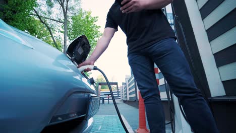 proceso de reabastecimiento de combustible de un automóvil eléctrico. un disparo debajo de la escotilla donde se carga el automóvil ecológico eléctrico. la escotella de carga del automóvil eléctrico se abre automáticamente. una mano masculina inserta un automóvil erecto