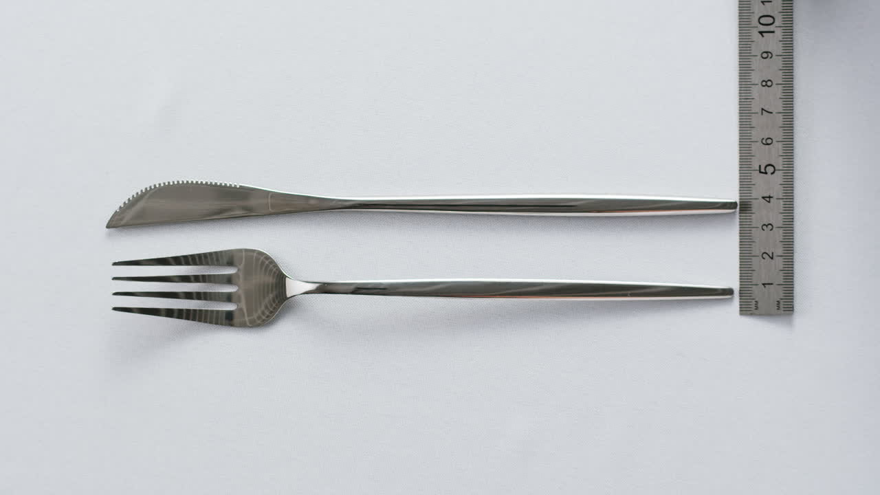 Minimalist table setting with white plate, fork, and knife arranged neatly, and a gloved hand adjusting cutlery.