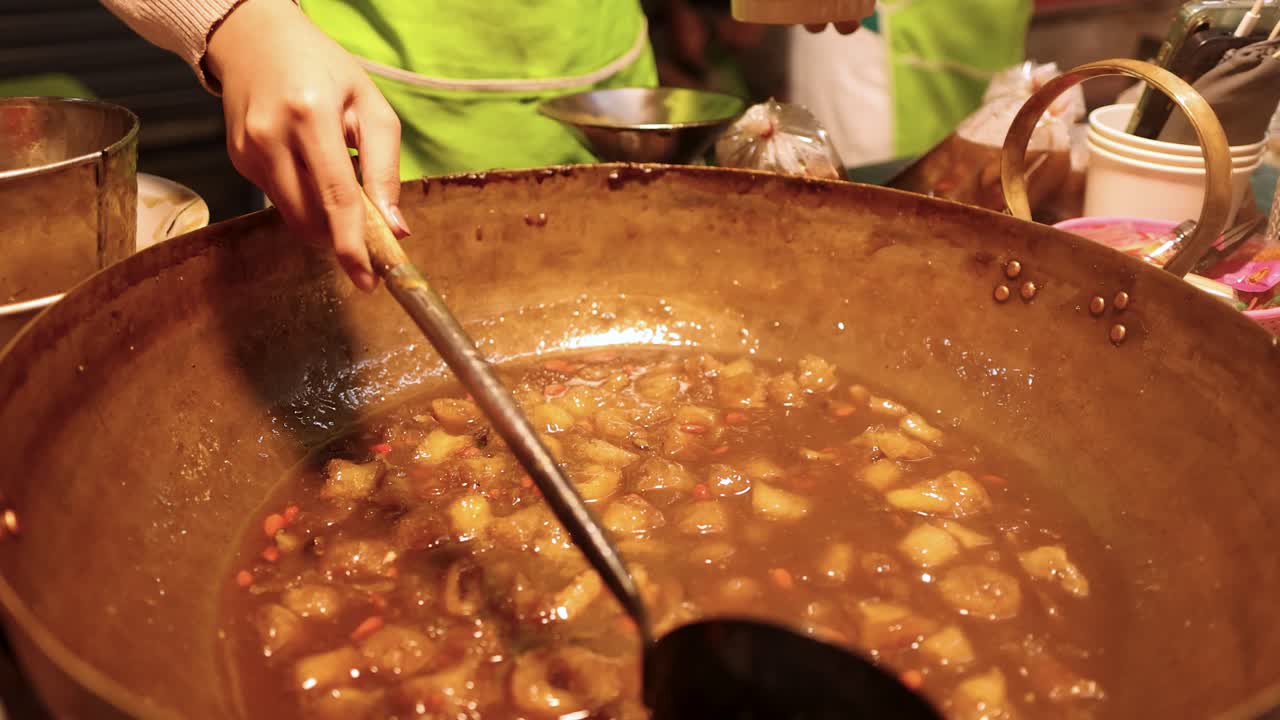 Vendor ladles steaming fish maw soup from large pot under warm street food lighting