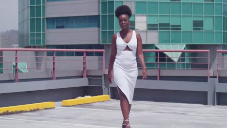 a black girl, dressed in white, walks on a rooftop overlooking the city skyline