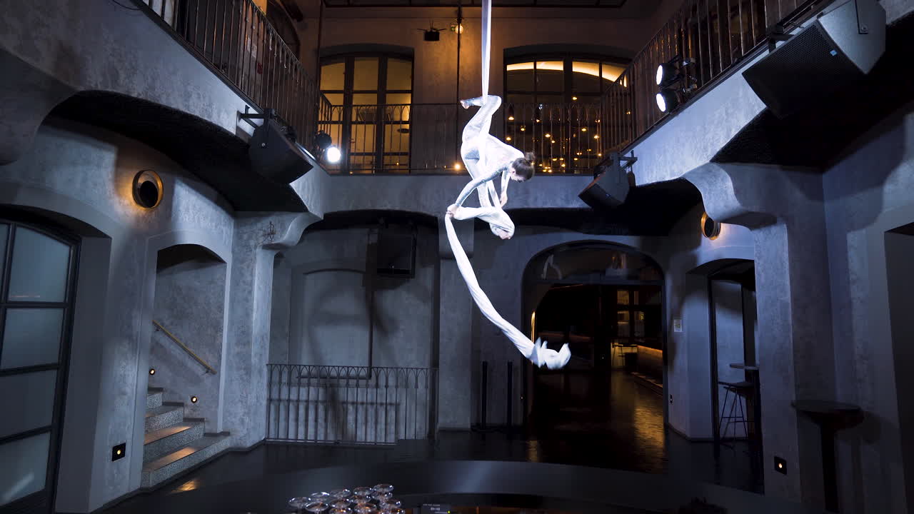 바 위의 실크에서 세로로 갈라지는 여성 공중 곡예사