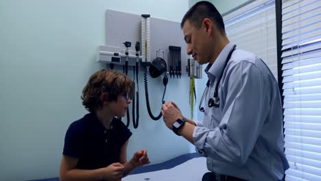 vista lateral de un joven médico asiático aplicando un vendaje en el brazo de un paciente caucásico en la clínica 4k