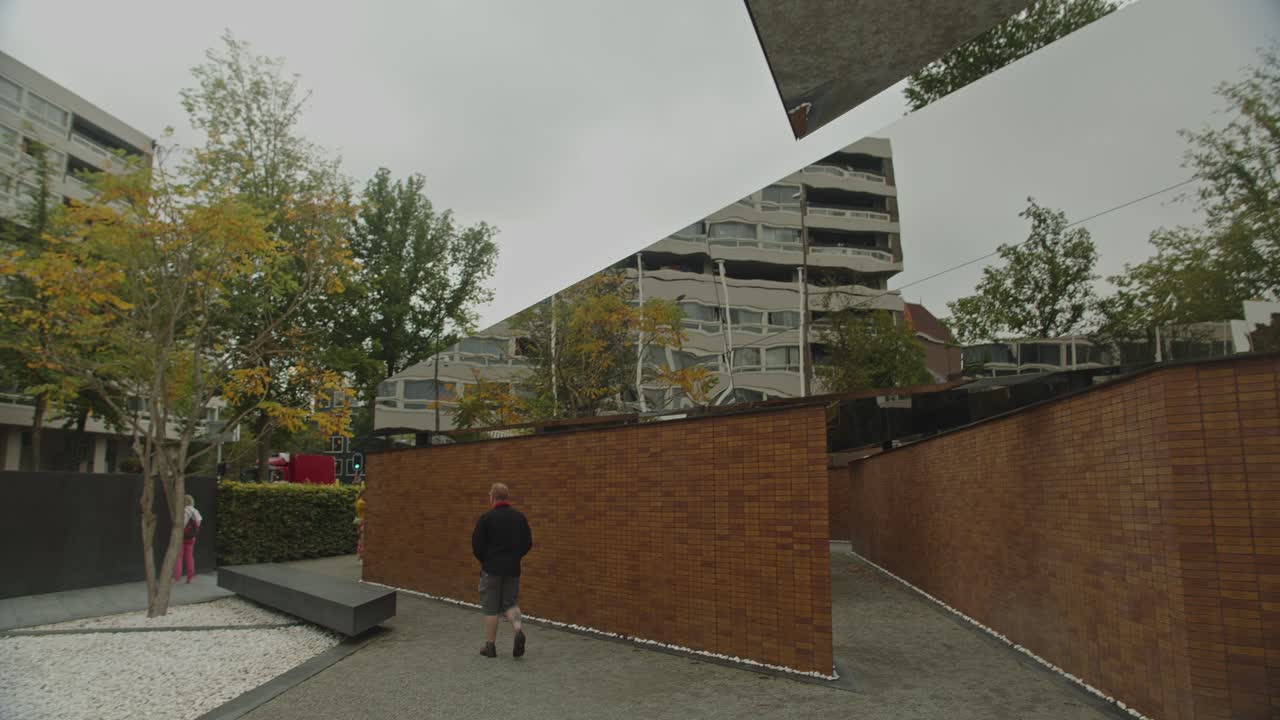 Tilt down towards person walking in reflective mirror at the National Holocaust Names Memorial in Amsterdam, the Netherlands
