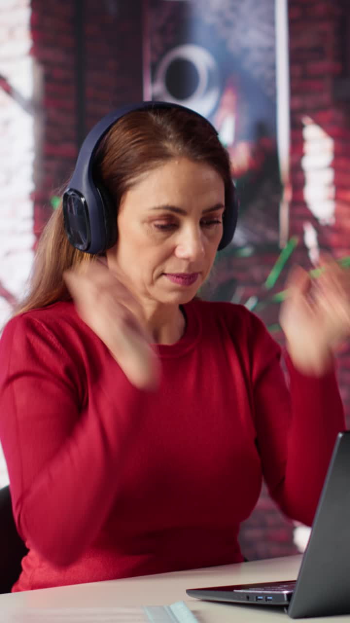 Vertical Video Mature person having fun solving her work tasks with headset on at desk