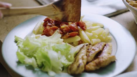 sirviendo almuerzo con pasta, filete de pollo, ensalada y salsa de tomate