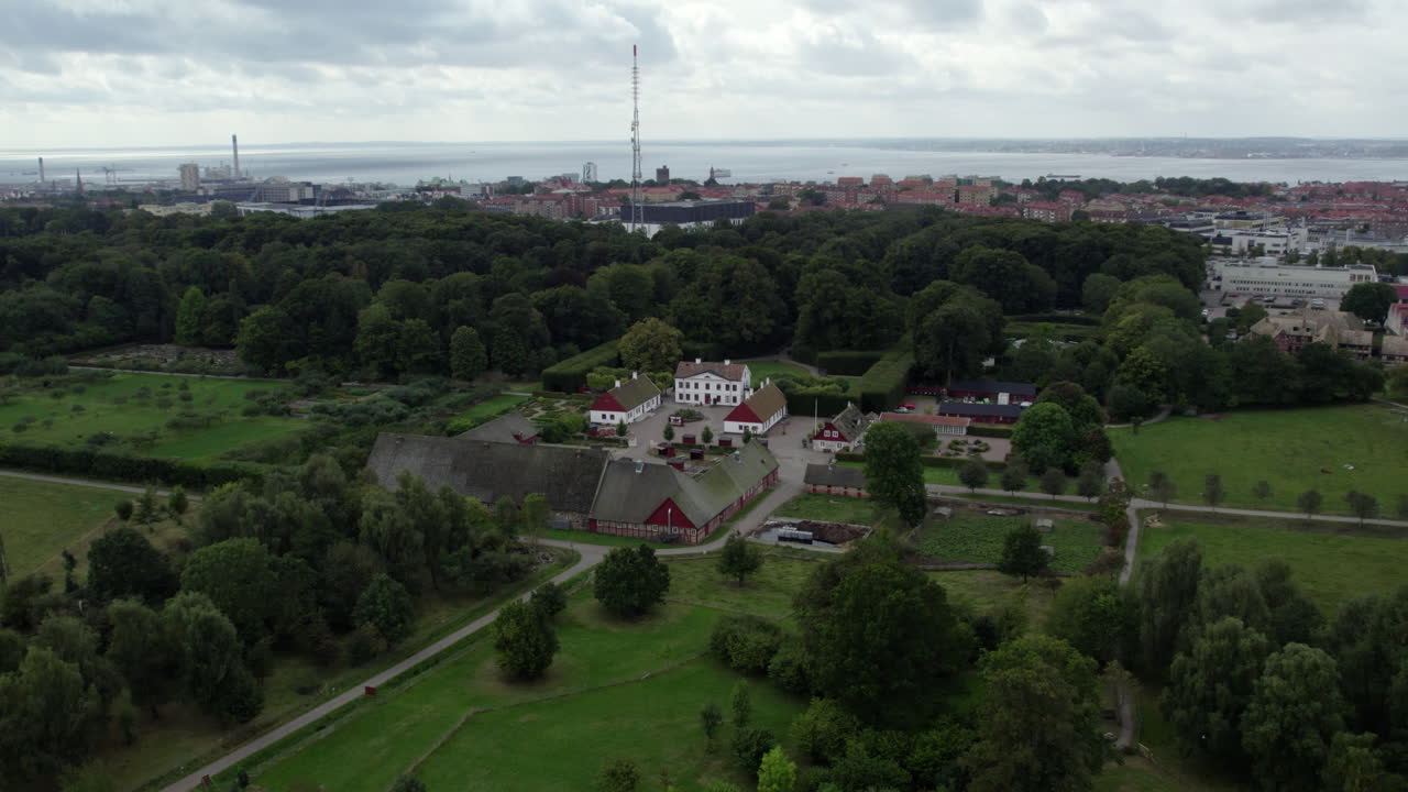 Fredriksdal Museum and Gardens, Helsingborg, Sweden - A Wide View of a Historic Estate Sits Surrounded by Dense Trees, Open Fields, and a Distant Coastal City - Drone Flying Forward