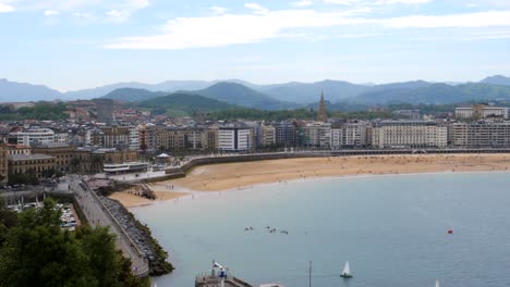 Aerial-panorama-shot-of-historic-city-of-San-Sebastian-with-sandy-beach-and-mountain-range-in-background