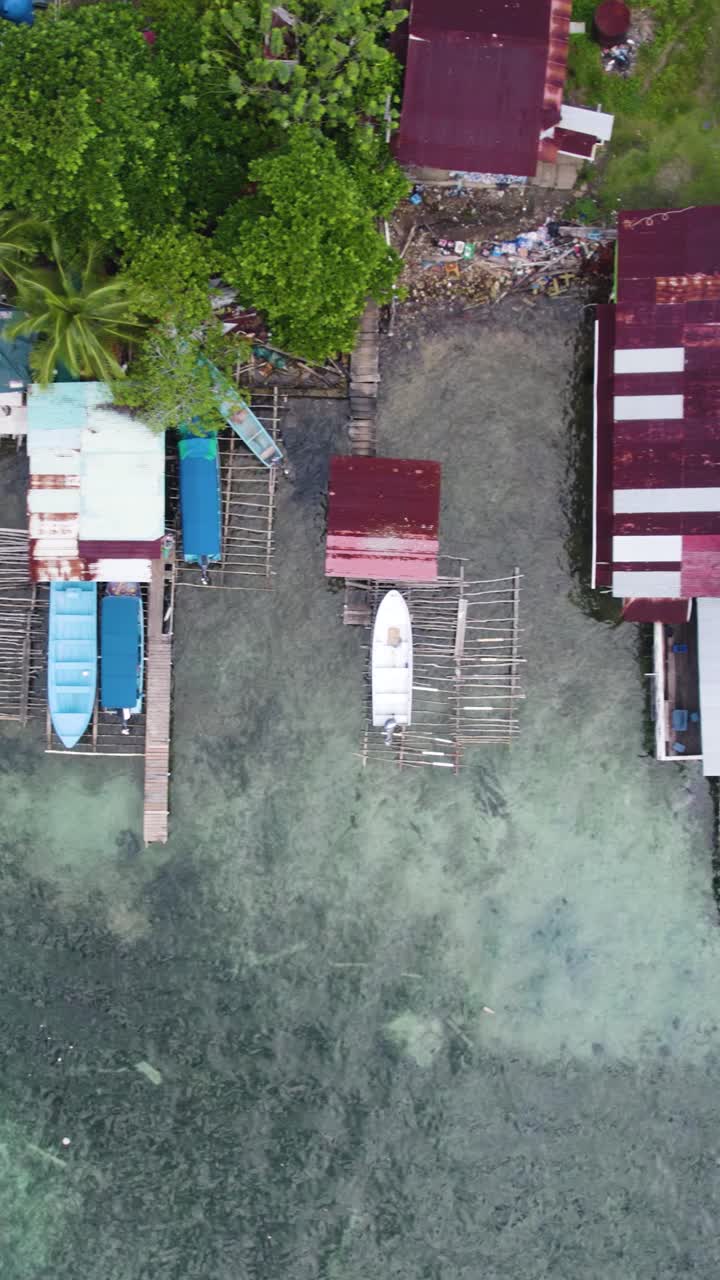 Vertical aerial birds-eye view of colorful boats docked along the shoreline of Bastimentos Island in Bocas del Toro District, Panama