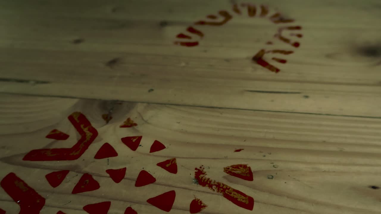 Slow motion low angle closeup glides over blood stained boot print, footprint pattern stamped on wood flooring. Trace of criminal intruder leaving the crime scene of violent break-in in dimly lit room