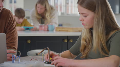 padre ayudando a su hija adolescente con un proyecto de electrónica sentado en la mesa de la cocina en casa con una computadora portátil - filmado en cámara lenta