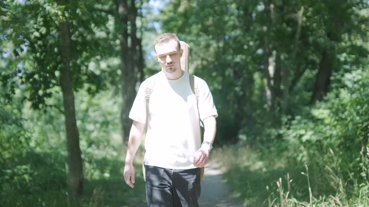 숲 근처의 거리에서 기타를 들고 는 젊은 남자