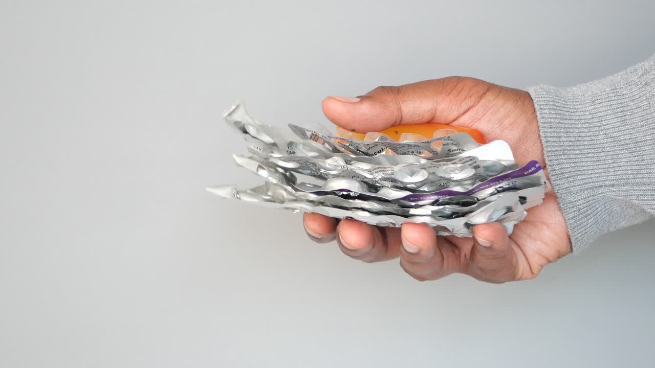 Eine Hand hält einen Stapel leerer Pillenflaschen und -packungen
