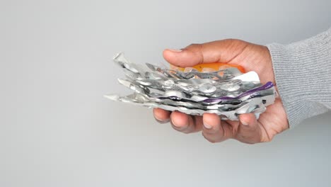 una mano sosteniendo un montón de botellas y paquetes de pastillas vacías.