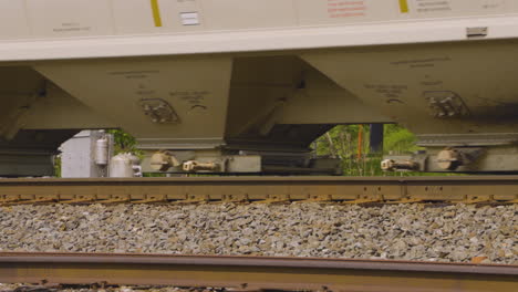 close shot of the wheels of a train with graffiti covered boxcars and hopper cars rolling along the rusty railroad tracks