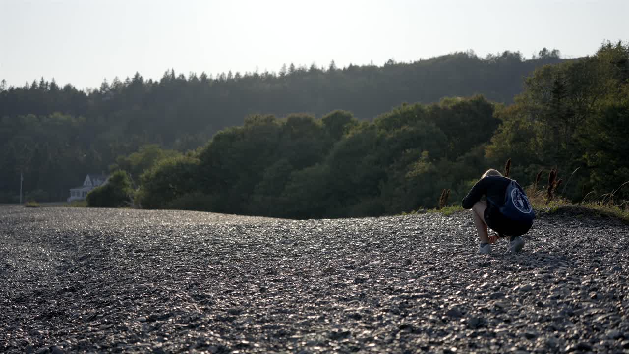 Woman bent down exploring and picking up interesting rocks from a stone beach
