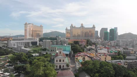 rising drone reveal shot of taipa skyline in macau with park and church in foreground and casino hotel in background