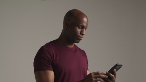 studio shot of smiling mature man with mobile phone getting good news against grey background