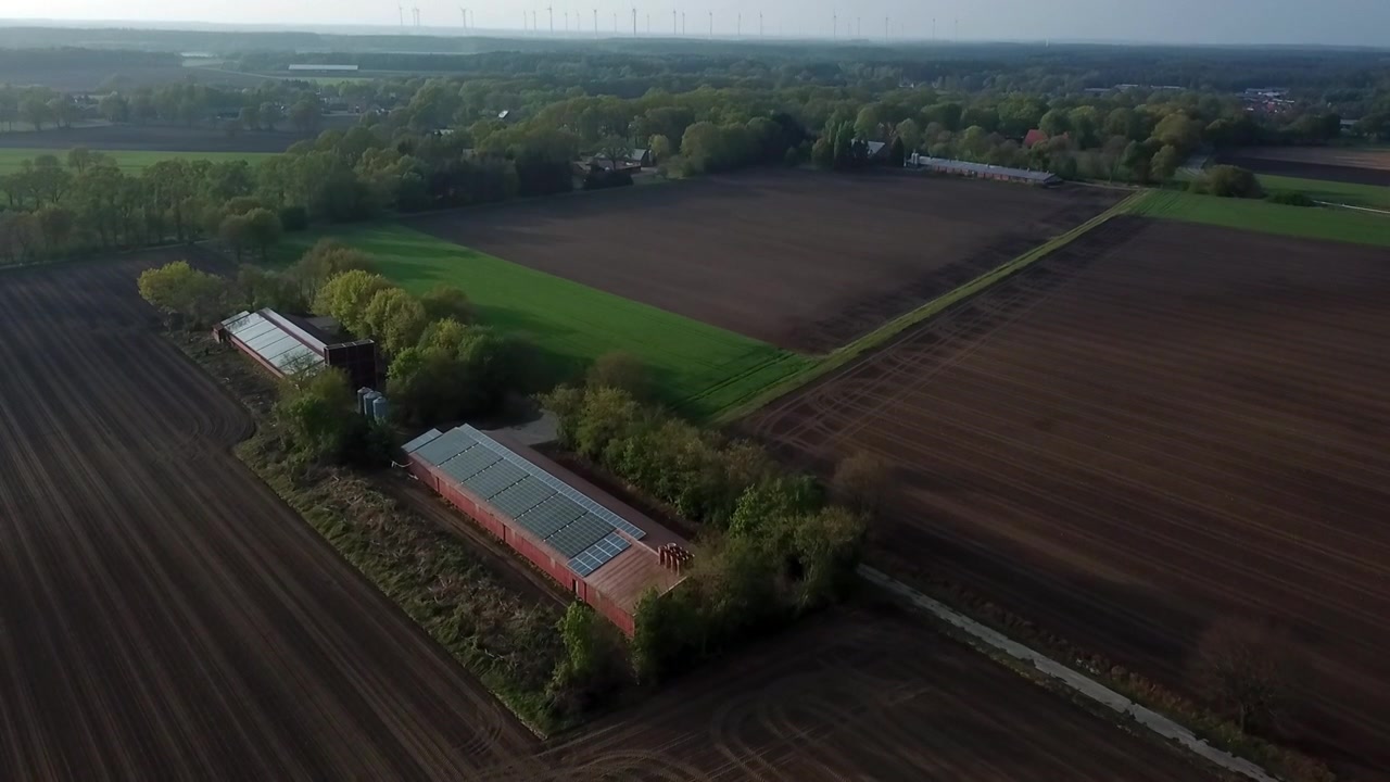 Luftfoto af tom, høstet landbrugsjord i landdistrikterne på en overskyet dag, der vipper op for at afsløre en lade på velplejet landbrugsjord og tåget baggrund