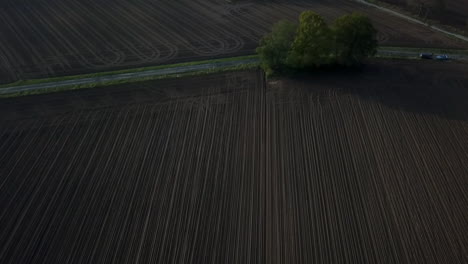 Aerial-view-of-empty-harvested-farmland-in-the-rural-countryside-on-an-overcast-day,-tilt-up-to-reveal-barn-on-a-groomed-farmland-and-misty-background