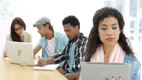 mujer usa la tableta mientras los colegas trabajan detrás de ella