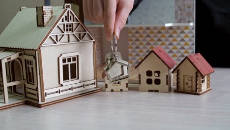 keychain with the keys to the new apartment in your hand. plywood toy houses on the table. purchase of real estate