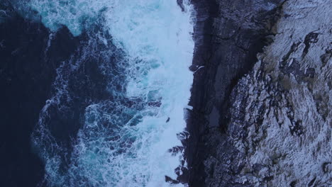 ocean waves crashing into steep rocky cliffs at winter