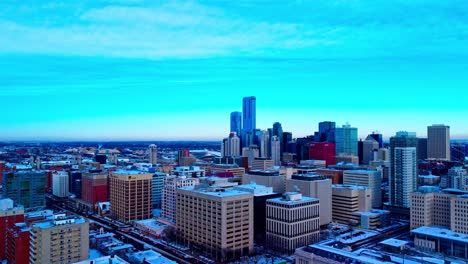 Vuelo-Aéreo-Sobre-El-Lado-Este-De-Los-Rascacielos-Del-Centro-De-Edmonton-En-El-Tercer-Día-De-Nieve-En-Noviembre-De-2021-Con-Un-Cielo-Azul-Claro-Con-Vistas-A-Oficinas,-Edificios-Gubernamentales-Y-Apartamentos-Residenciales