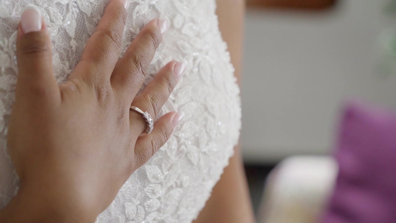 Hand with engagement ring rests gently on white lace bridal dress, close-up view
