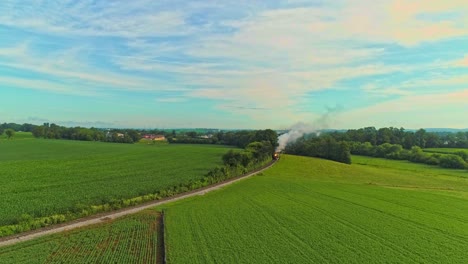 Paisaje-Aéreo-De-Tierras-De-Cultivo-Y-Un-Motor-De-Vapor-Antiguo-Pasa-A-Través-De-Los-Campos-De-Maíz-En-Una-Mañana-De-Verano-Temprano