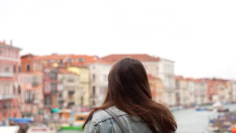 tourist takes of hat, fixing hair while enjoying view on grand canal, venice