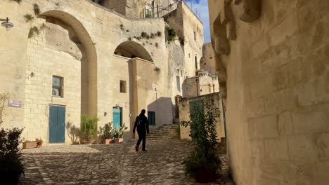 Man-walks-in-shadow-of-tall-brown-building-facade-in-old-city,-Italy,-static