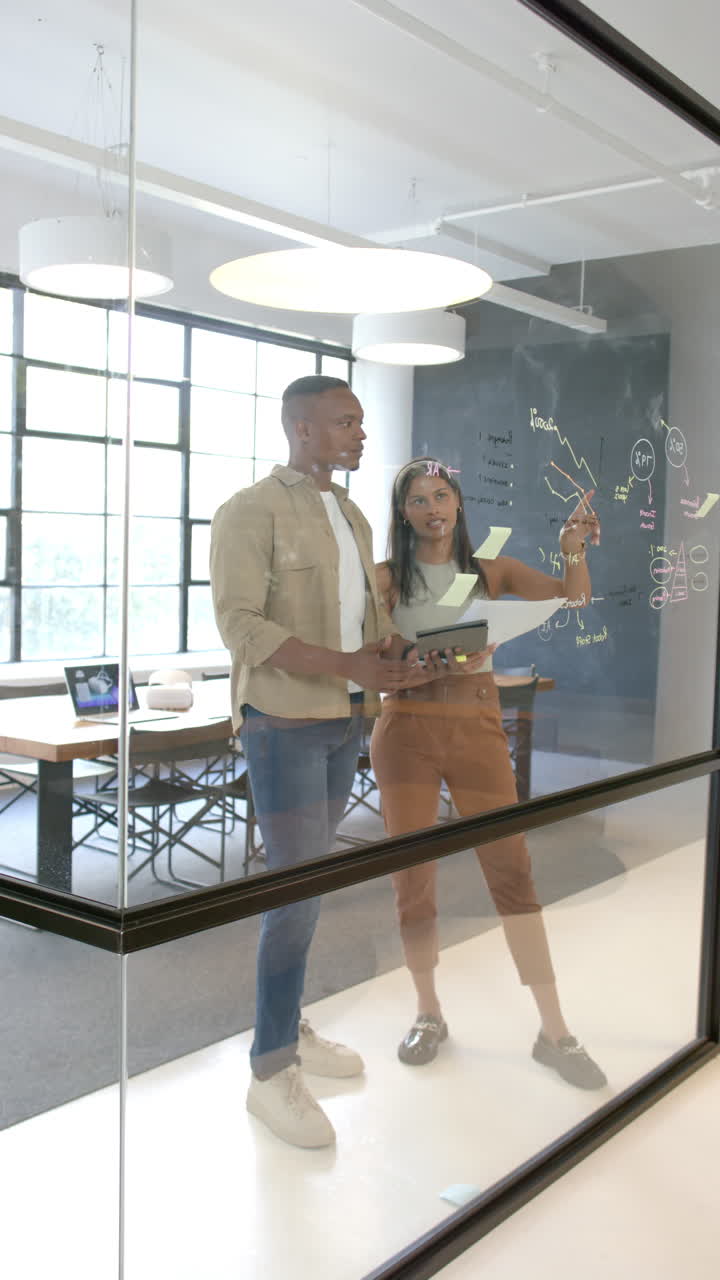 Vertical video: Collaborating in office, colleagues brainstorming and writing on glass board