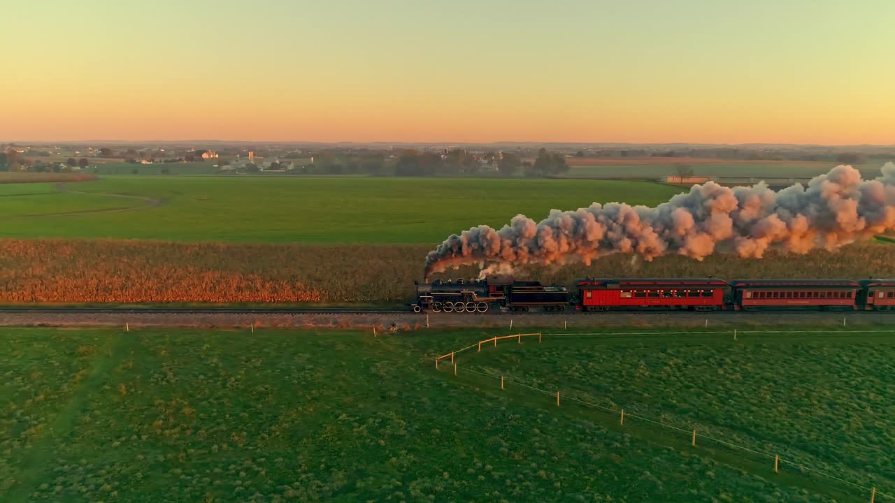 황금빛 일출에 증기기관과 객차의 공중 전망, 증기와 연기가 농지를 가로질러 이동하는 모습