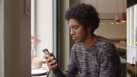 young man using mobile phone to update social media in cafe