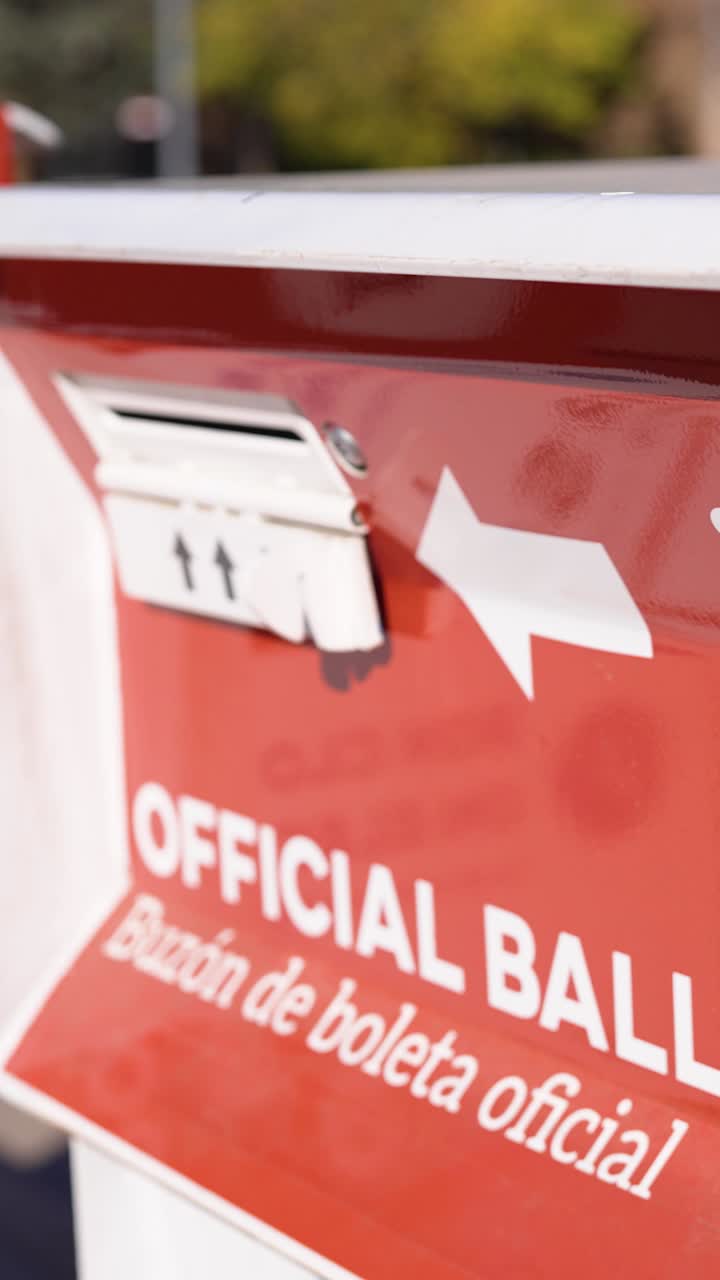 Inquadratura verticale di un'urna elettorale con segnaletica ufficiale, che mostra la consegna delle schede, l'accesso pubblico al voto e la partecipazione democratica