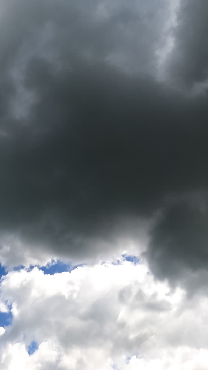 White and grey clouds forming in the blue sky. Rays of sun breaking through the clouds timelapse. View from below. Vertical video