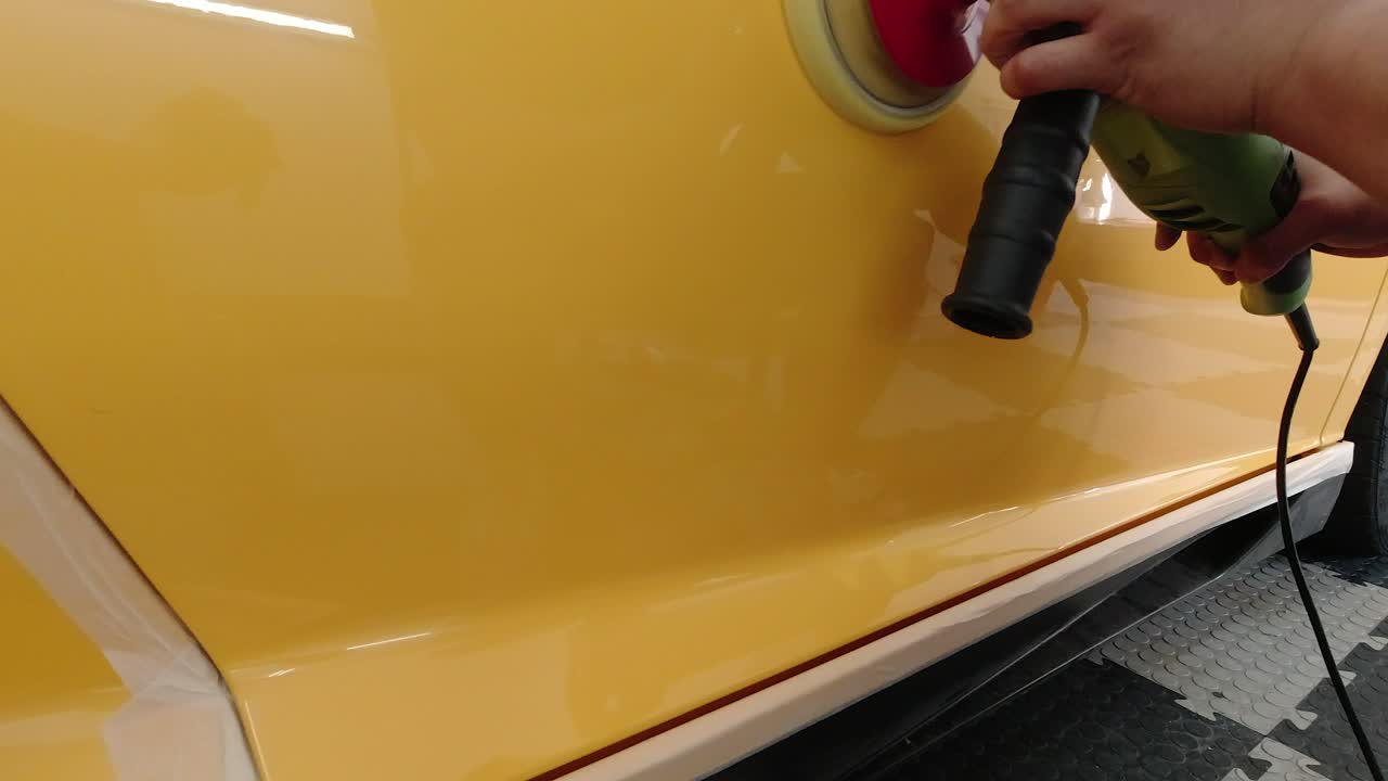 Yellow supercar's panel being polished with rotary machine in slow motion