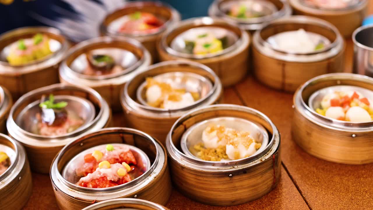 Hands skillfully arrange steamed dim sum in bamboo baskets at a vibrant Phuket market. Warm lighting enhances the colorful presentation
