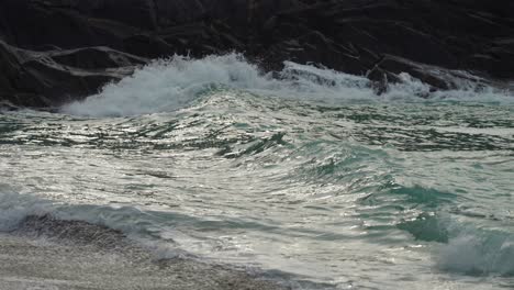 A-close-up-shot-of-the-low-tidal-waves-crashing-on-the-rocks-and-spilling-on-the-sandy-shore