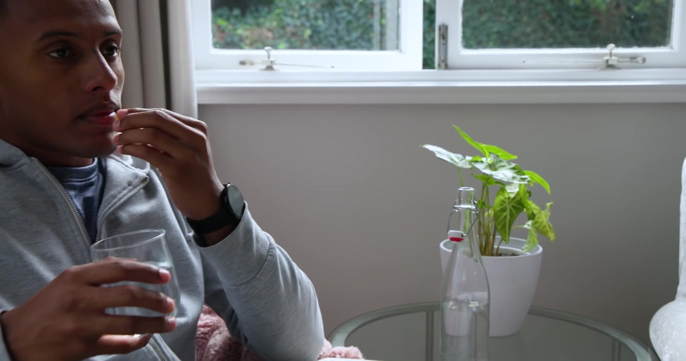 Uomo afroamericano che vede pillole gialle su un tavolino, allunga la mano e prende la medicina con acqua