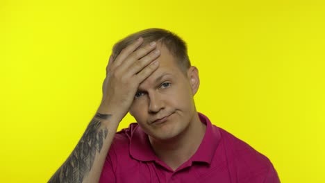 portrait of young caucasian man posing in pink t-shirt. dissatisfied guy puts hand on face, facepalm