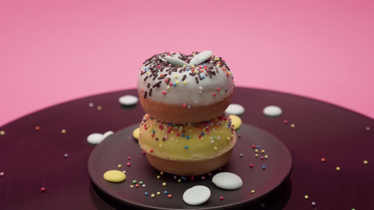 Choco crumbs fall on two chocolate American donuts topped with yellow and blue chocolate