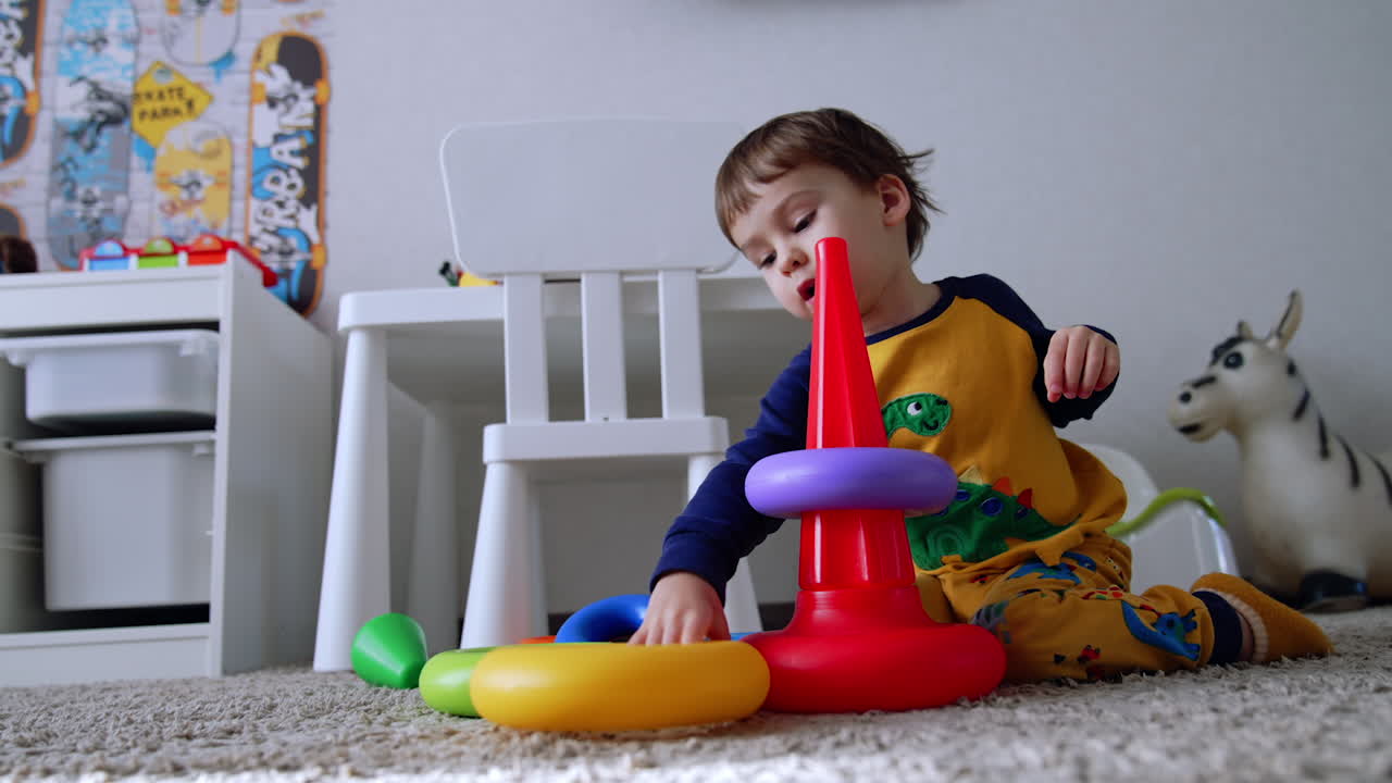 Two year old toddler sitting on the floor. Little kid assembles the pyramid and stands up.