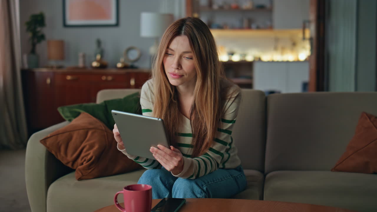 Woman touching tablet screen at home sofa. Girl using computer for online work