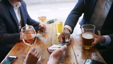 close up of businessman paying for round of drinks in bar after work using contactless card