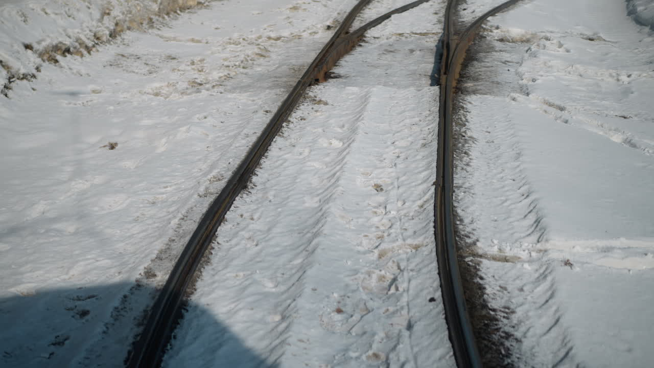 view from fast train shows snow covered curved rails, steel lines sweeping through winter cutting frosty embankment, crisp sun highlights texture and footprints on packed track bed